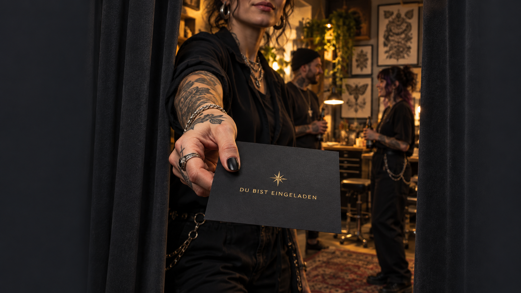 Eine tätowierte Person reicht dir eine Karte mit der Aufschrift Du bist eingeladen. Hinter dem geöffneten Vorhang treffen sich kreative Menschen im Tattoo-Studio.